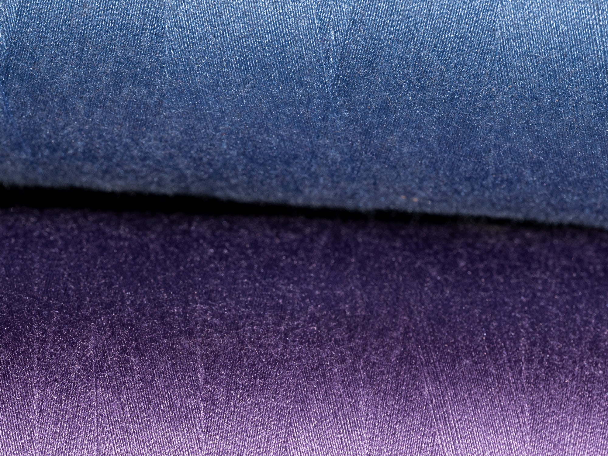 Macro detail of denim-weight fabric fading from indigo blue to violet