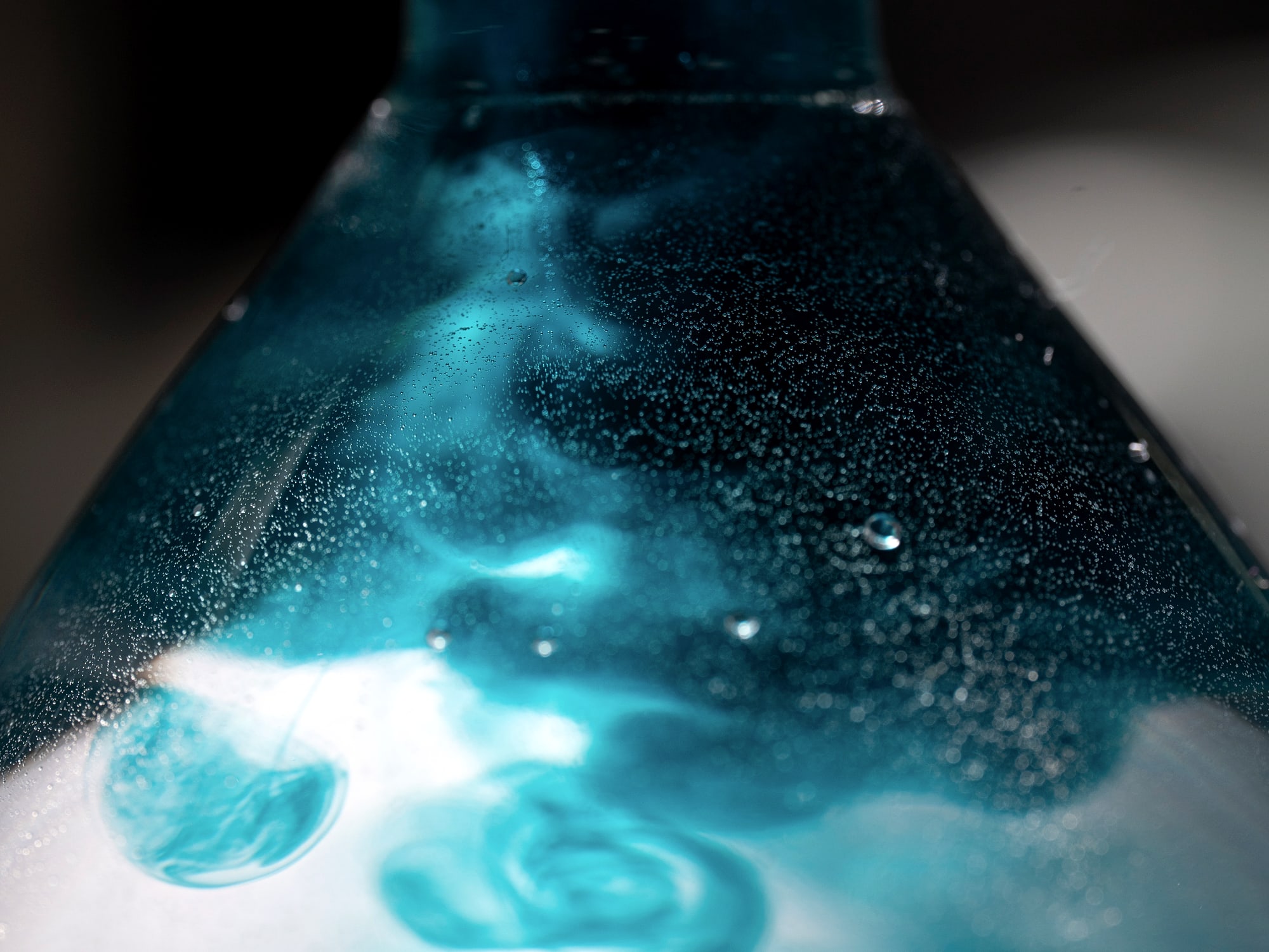Close-up of teal dye developing and foaming inside a glass lab flask