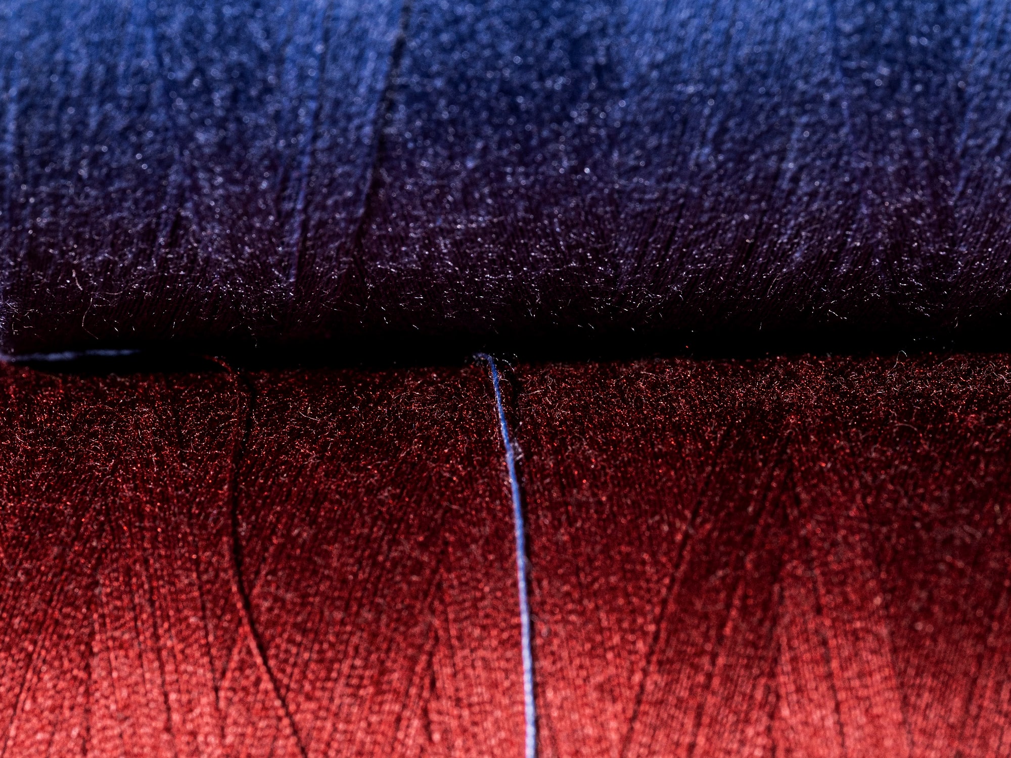 Two yarn cones side by side, one blue and one burgundy, with a single pale thread strung between them