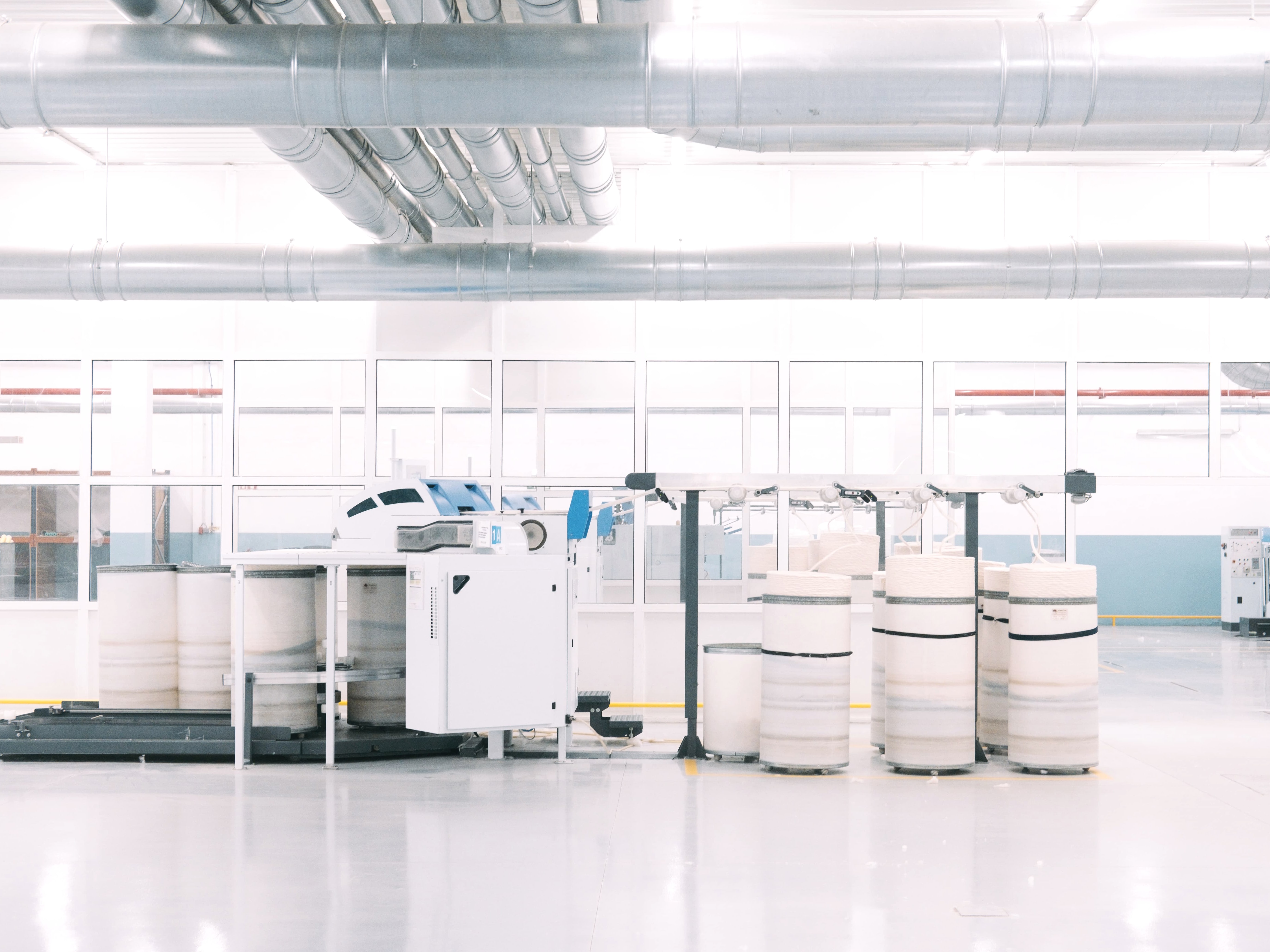 A production floor with overhead ducting and rows of wound yarn cones